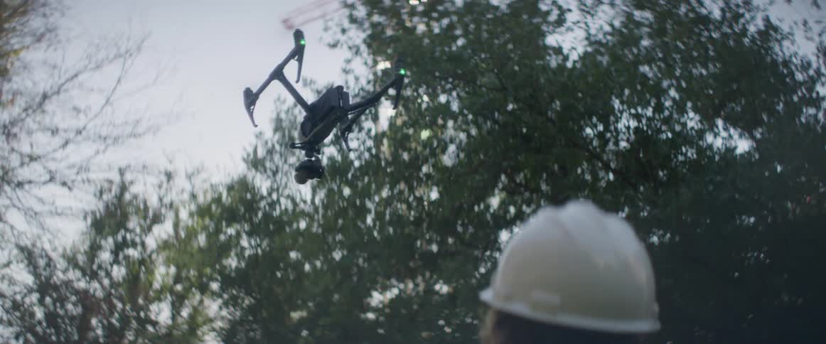 A construction worker stands at a construction site and flies a drone in to the air
