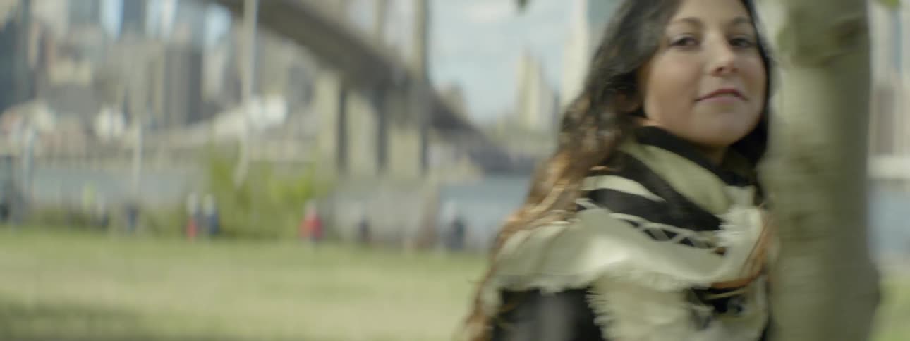 A woman is walking outside with a city behind her on a sunny day