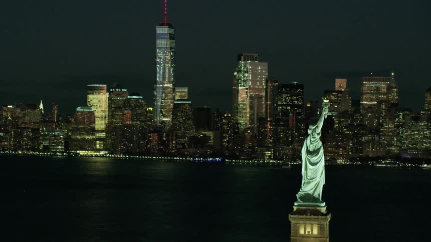 The statue of liberty with the nighttime skyline of new york city in the background