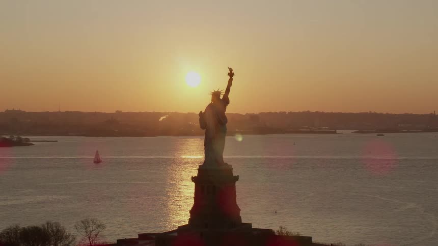 The statue of liberty looming over the ocean in the evening