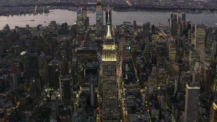 Aerial view of illuminated high rise buildings and skyscrapers with spires next to river in city at dawn