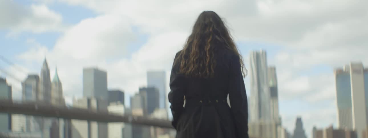 A woman stands outside in front of a bridge and city skyline