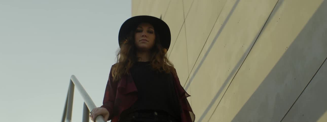 A woman wearing a hat walks down a narrow set of stairs outside