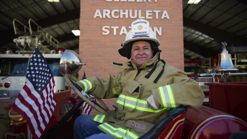 A fireman sits in a retro fire engine while smiling into the camera