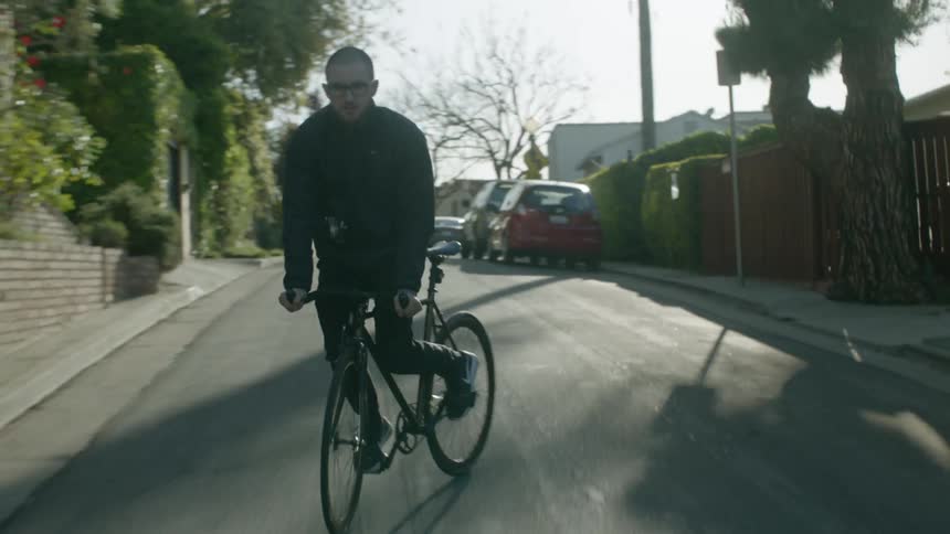 Man bicycles down sloping street through neighborhood briefly turning bike side to side