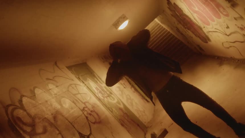 A man holding his head in a hallway with graffiti on the walls with stairs in the background