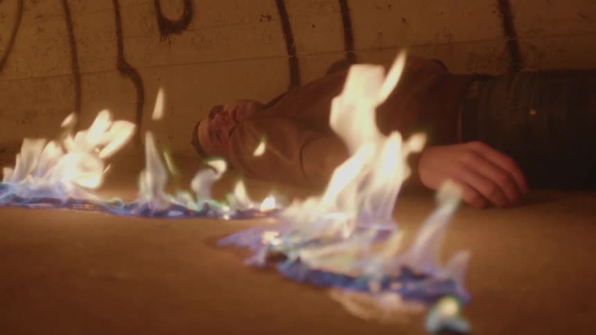 A man is lying unconscious on the floor and an electrical cord near him is on fire