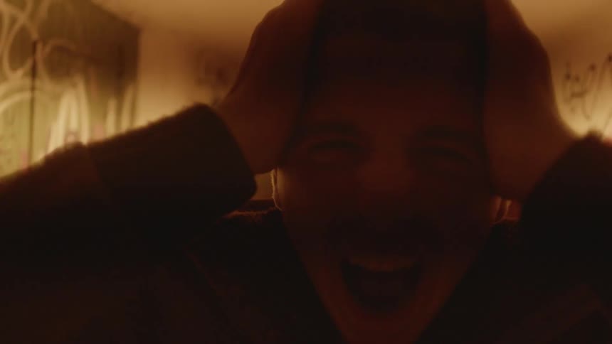 Young man standing on a dimly lit hallway with his hands over his head screaming