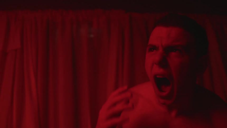 A man grabs his head and screams as he stands in a room with flashing lights