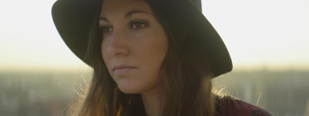 A woman wearing a floppy hat stands outdoors in the sunlight