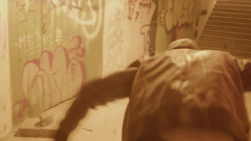 Young man wearing a leather jacket crawling on the floor of a corridor stands up shielding his face from the lights