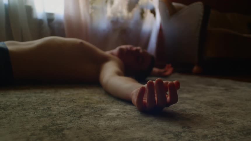 Shirtless man lies down on the ground moving his fingers in the living room