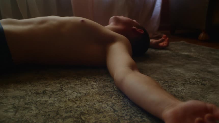 A man laying on the floor on a rug in a room with a window in the background