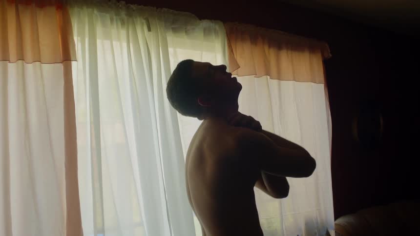 Young muscular shirtless man hughs himself inside a dimly lit room at home