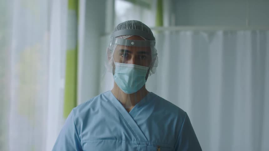 Health care provider wearing a face mask and shield standing in a hospital room