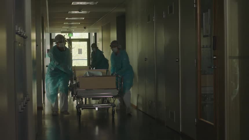 Medical personnel wheel two gurneys with patients down a long hallway