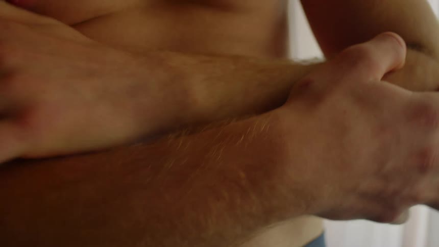 A man hugs himself by the window