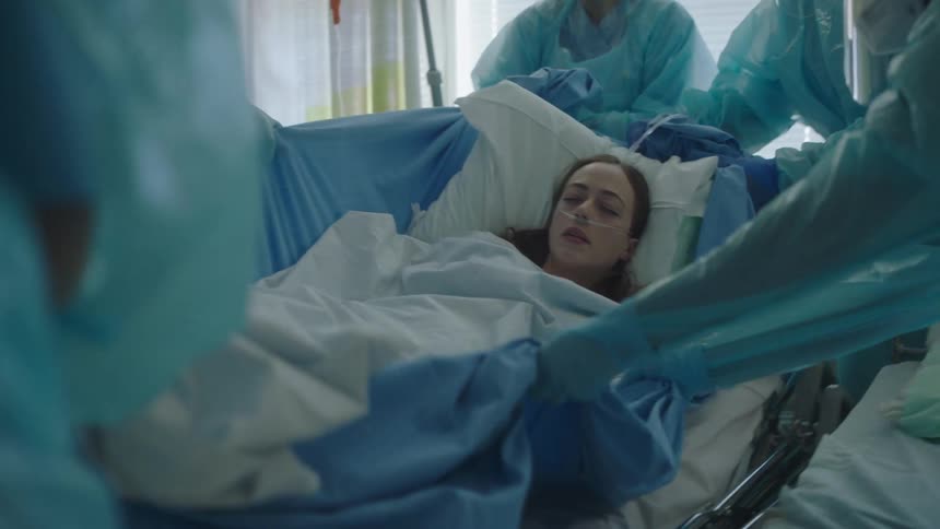 Medical staff work together to lift and place an unconscious woman in a hospital bed
