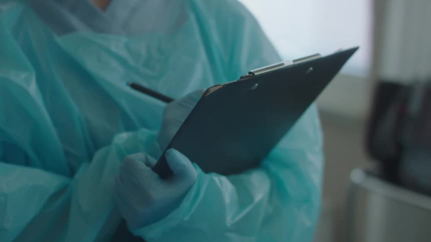 A person wearing hospital scrubs is writing on a clipboard
