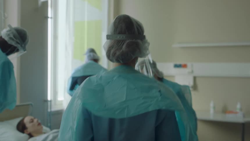 Nurse walks past medical supplies joining other medical personnel working around patient lying on hospital bed