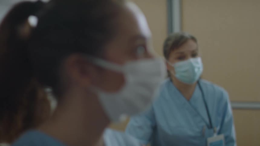 Nurse exchanges glances with another nurse nodding at another person during medical personnel meeting