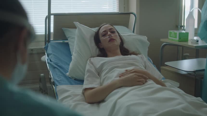 A woman is lying in a hospital bed as a nurse is in the room with her