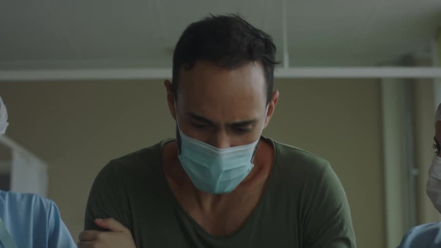 Doctors helping a patient wearing a face mask to stand up from the hospital bed