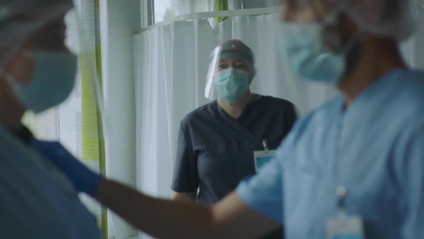 Doctors and nurses wearing protective personal gear talking on a hospital room