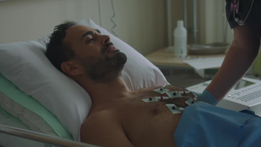 Nurse comforts male patient lying on his back with sensor pads attached to his bare chest