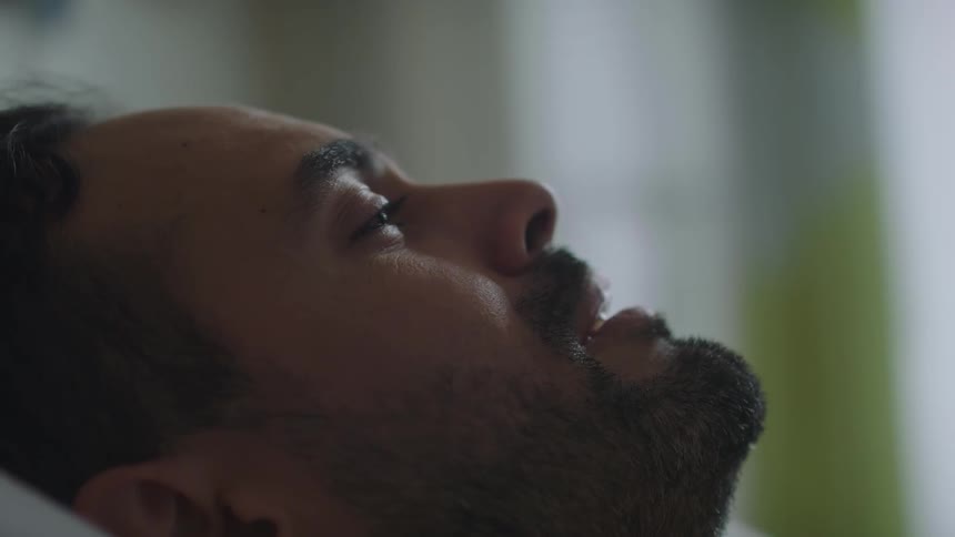 Young sad bearded man cries while resting on a bed inside a room
