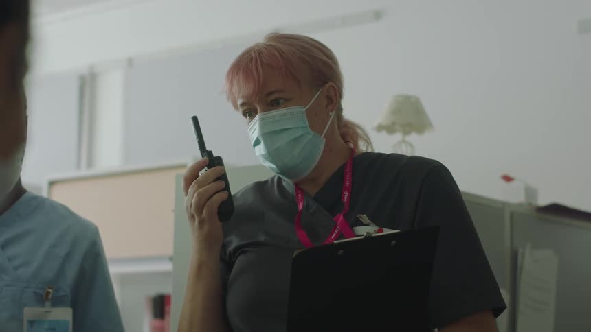 Two nurses use a walkie talkie to talk with someone as they speak with a patient