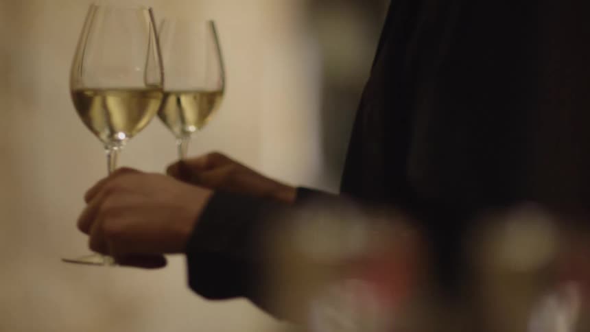 A person hands two people a glass of white wine