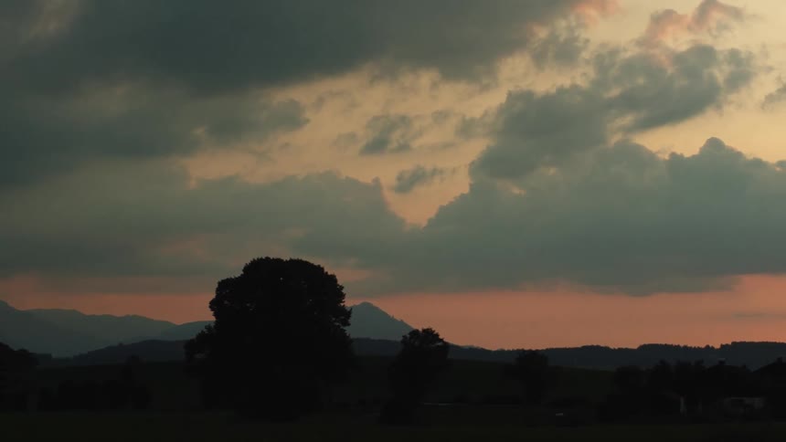 Silhouettes of trees and a mountain range under a pink and blue sky