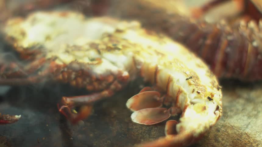 Person uses metal spatula to flip lobster half cooking on metal grill
