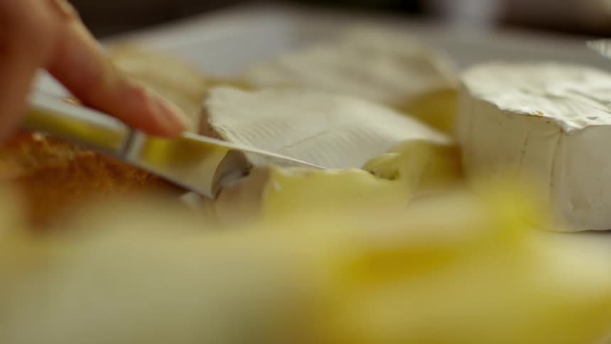 Someone is using a knife to cut a piece of brie