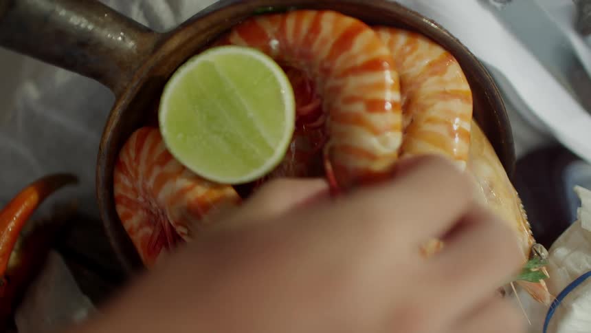 A person taking shrimp from a pan on a table