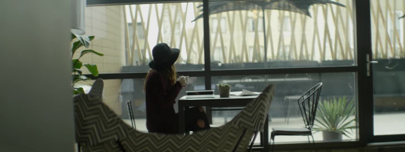 A woman sits at a table drinking from a mug