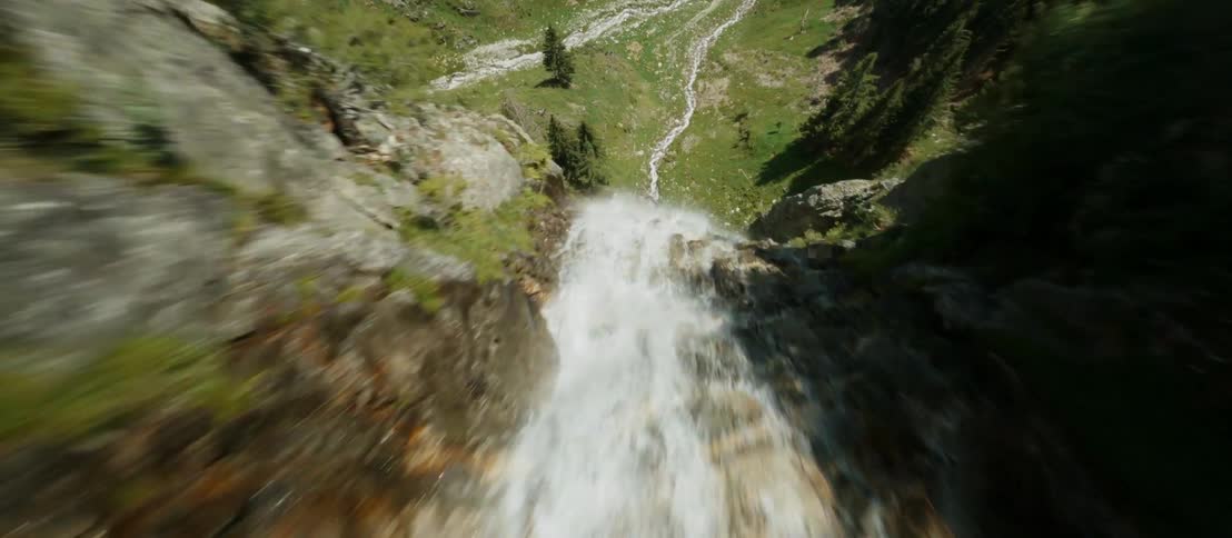 River churns through rapids and waterfall down steep cliff before crossing gap between conifer forests