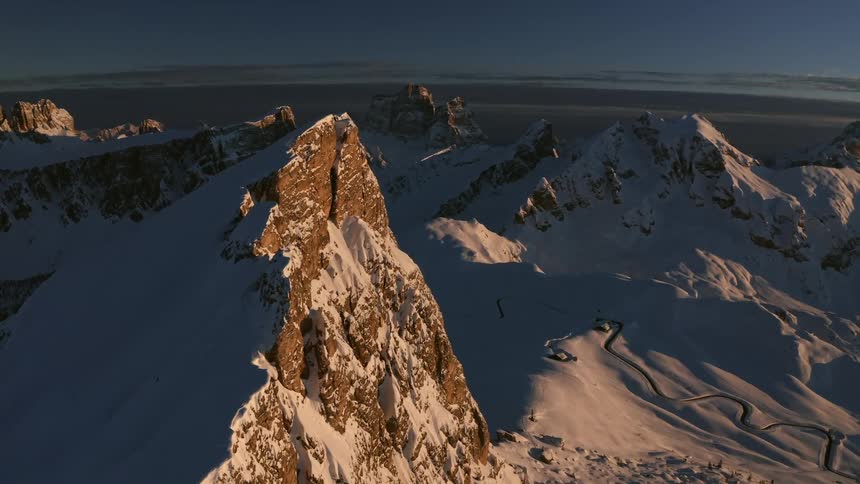 Aerial view of the snow covered slopes and peaks on a mountain range at sunset
