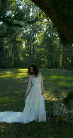 A bride in a lace gown is standing under a tree posing for a picture