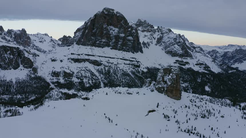 Cloudy sky over mountain peaks partially covered in snow after sunset