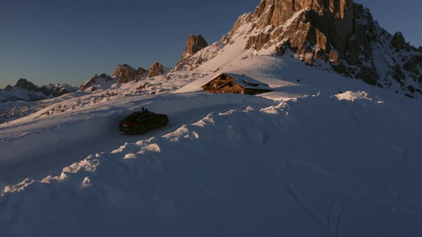 A car travels up a snow covered mountain road with a passengers head and camera through the sunroof