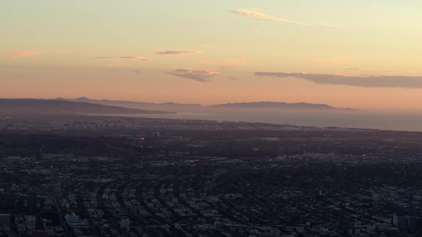 Large town sprawls toward mountains on horizon on foggy day under a red sky