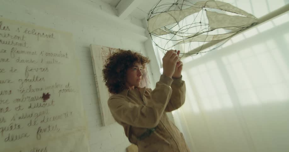 A woman in a room fixing a mobile with a wall a window and curtains in the background