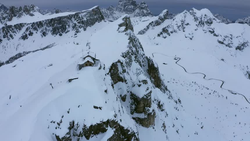 A building on top of a jagged mountain ridge in the snow covered wilderness