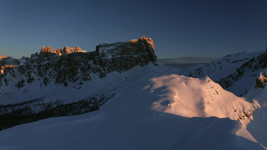 The sun is rising over snow covered mountain peaks and rocky cliffs in the wilderness