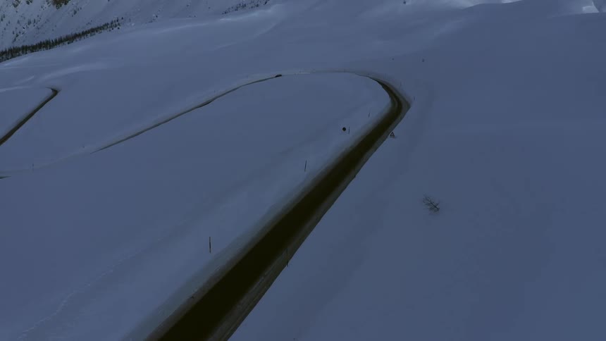 Very deep snow lines a roadway as a vehicle makes its way on the winding path