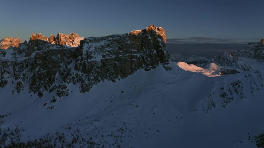 Aerial view of snow covering the slopes of a mountain range at sunset