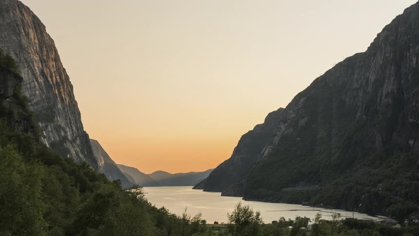 A river flows along the floor of a narrow mountain valley as the sun sets