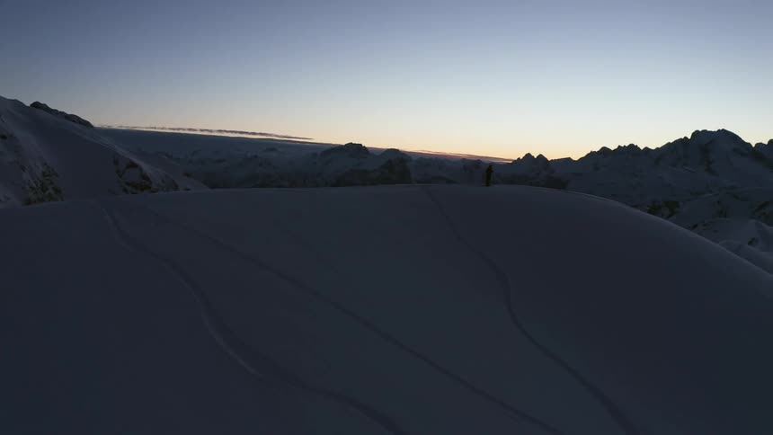 Aerial view of man standing on snowy mountain and snowy valley being silhouetted against the sky at dawn